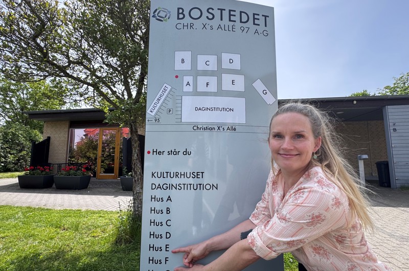 Afdelingsleder Charlotte Onsberg Hansen foran Bostederne Skilt peger på hendes afdelinger