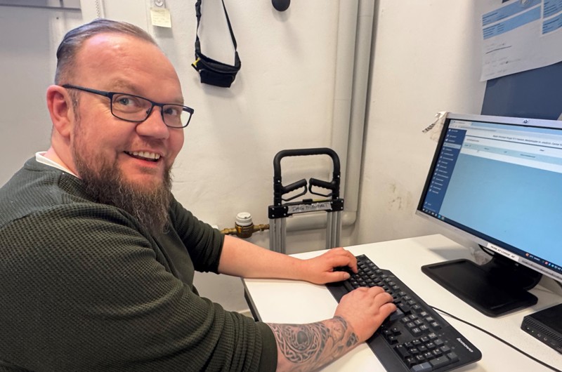 Mads Christian Hansen sidder ved computer og smiler